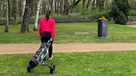 Eine Frau zieht einen Wagen mit Golfschlägern hinter sich her.