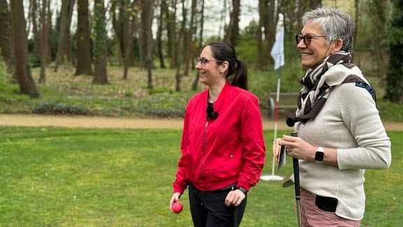 Zwei Frauen stehen lächelnd auf einem Golfplatz.