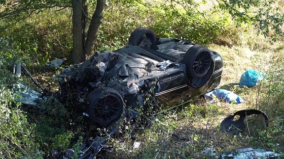 Ein demoliertes Auto liegt auf dem Kopf auf einem Feld. 