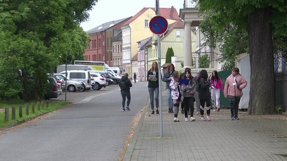 Kinder laufen auf einem Fußweg eine Straße entlang 
