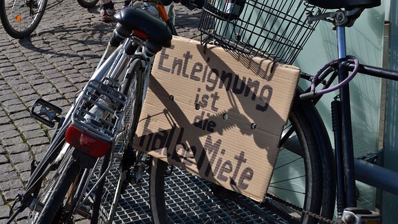 Pappschild "Enteignung ist die halbe Miete" an einem Fahrrad befestigt.