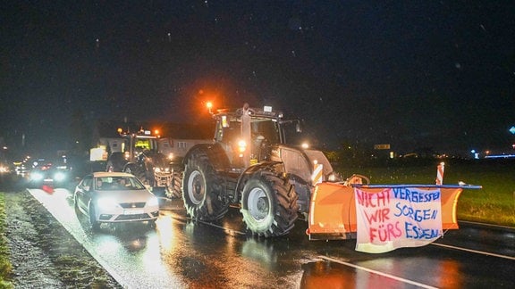 "Nicht vergessen wir sorgen fürs Essen" steht auf einem Transparent an einem Traktor, der auf einer Straße fährt.