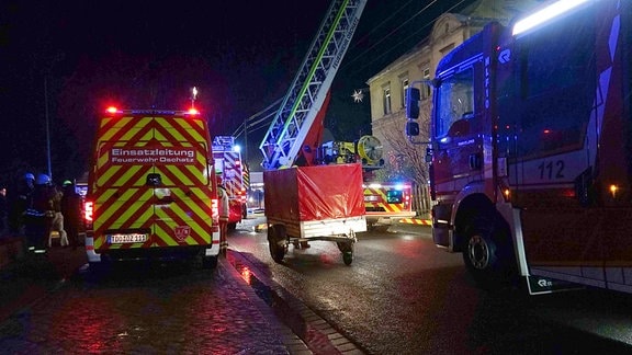 Feuerwehren stehen mit verschiedener technischer Ausrüstung in Dunkelheit vor einem Wohnhaus