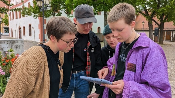 Eine Gruppe von jungen Erwachsenen steht auf dem Marktplatz von Grimma und schaut auf ein Tablet.