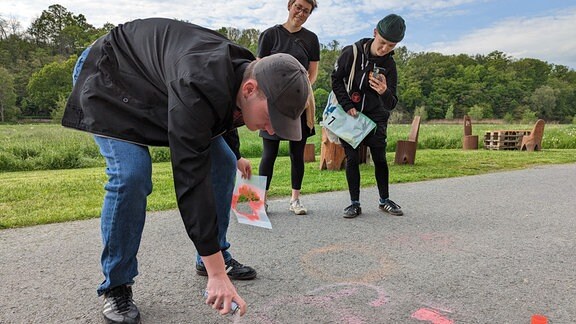 Ein junger Mann sprüht mit abwaschbaren Graffiti auf einen Fußweg.