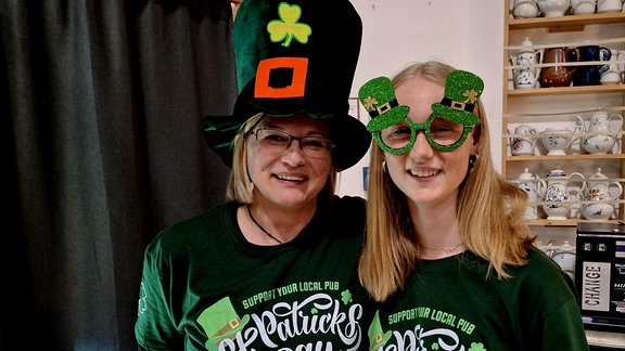 Zwei junge Frauen haben sich als Irlandfans in grüne Kleider und mit Hütern ausgestattet und lachen in die Kamera.