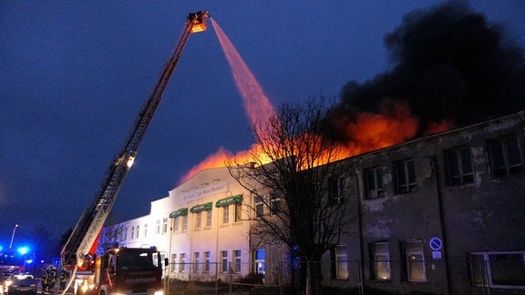 Feuerwehrleute löschen mit einem Löschkran ein Fabrikgebäude