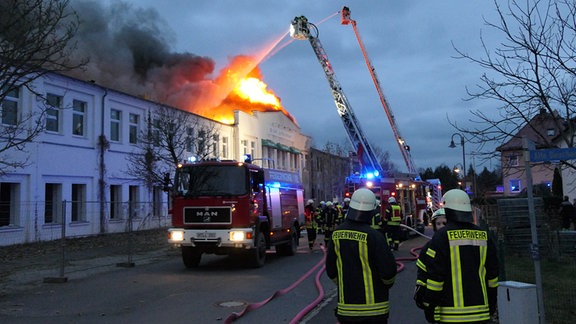 Feuerwehrleute löschen mit einem Löschkran ein Fabrikgebäude