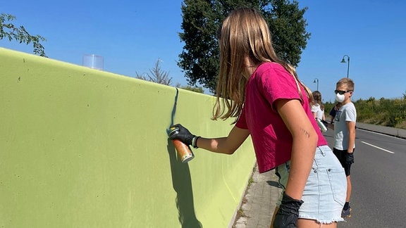 Ein Mädchen malt mit einer Spraydose an eine grüne Wand.