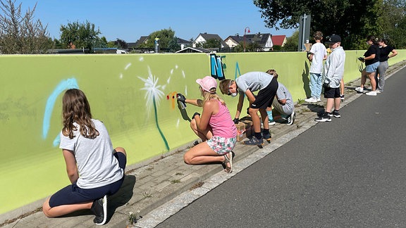 Kinder malen mit Spraydosen an eine grüne Wand.