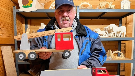 Ein Händler hält Spielzeug-Laster aus Holz in die Kamera.