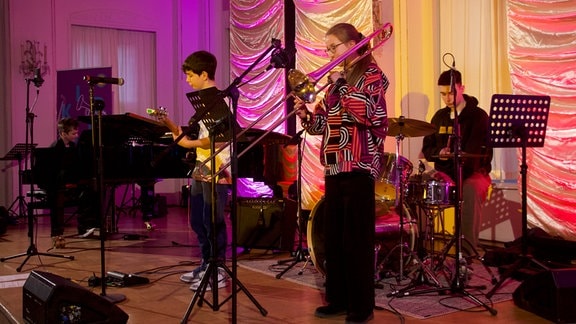 Das Rockytrio: vier Nachwuchsmusiker spielen auf einer Bühne Klavier, Posaune, Schlagzeug und Bassgitarre