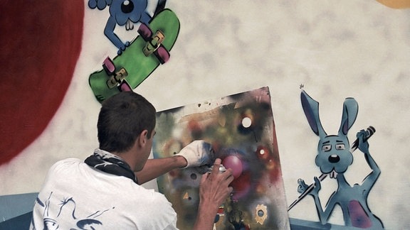 Ein Künstler benutzt Spraydose und Schablone an einer Wand.