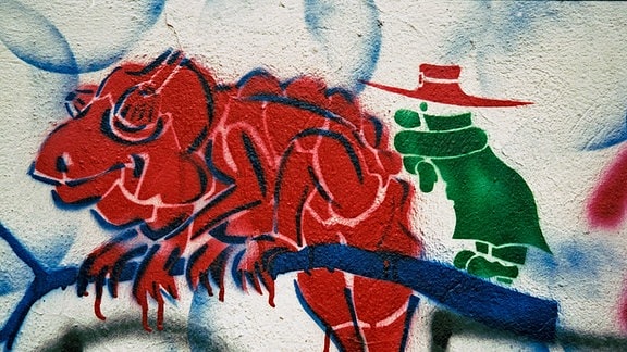 Ein Graffiti von einer grünen Figur mit rotem Hut neben einem roten, gesprühten Chameleon.