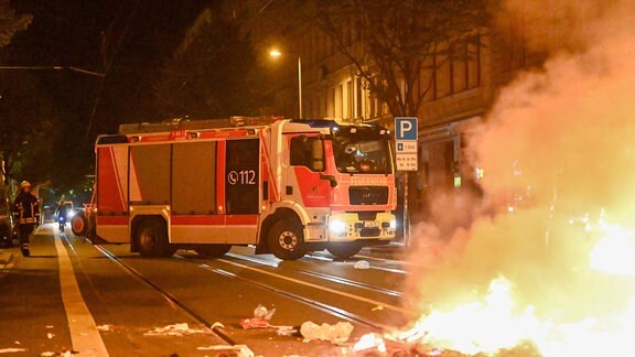 Auf einer Straße brennt Unrat, ein Feuerwehrauto steht im Hintergrund