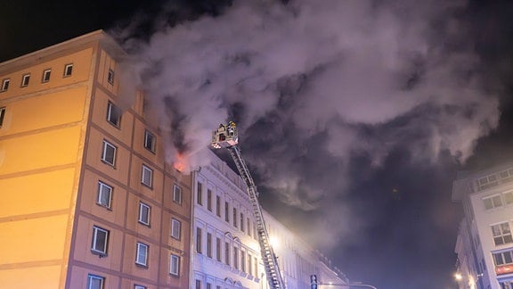 Viel Rauch dringt aus einer brennenden Wohnung in einem Mietshaus. Die Feuerwehr löscht mit Hilfe einer Drehleiter.