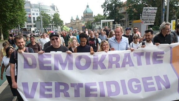 Teilnehmer einer Demonstration gegen Rechts im Vorfeld der Landtagswahl 2024, darunter Sebastian Krumbiegel (2.v.l.), Sänger, und Burkhard Jung (SPD, 3.v.r.), Leipzigs Oberbürgermeister, ziehen mit einem Banner mit der Aufschrift "Demokratie verteidigen" durch die Innenstadt.