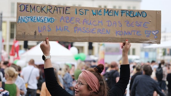 Eine Teilnehmerin einer Demonstration gegen Rechts im Vorfeld der Landtagswahl 2024 hält ein Plakat mit der Aufschrift „Demokratie ist wie mein Freund Anstrengend - aber auch das Beste was mir passieren konnte!“.