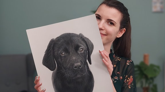 Eine Frau hält ein gemaltes Bild eines Hundes in der Hand. 