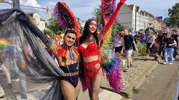 Neben einem Wagen posieren freudig zwei Dragqueens