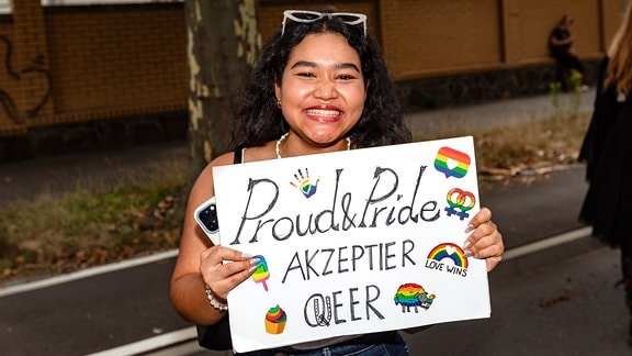 Eine junge Frau hält ein queeres Plakat.  