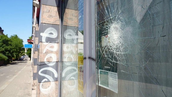 Zerbrochene Fensterscheibe an einem Gebäude, im Hintergrund ein Eingansschild: Polzei