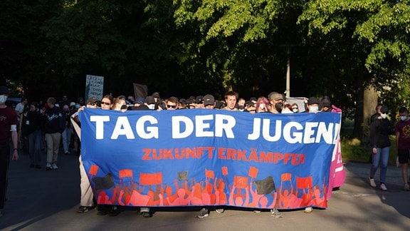 Teilnehmer und Teilnehmerinnen laufen in Leipzig bei der Demo unter dem Motto "Tag der Jugend" hinter Transparenten auf der Straße entlang.