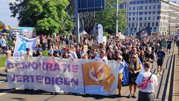 Hunderte Menschen mit Transparenten laufen über eine mehrspurige Straße in Leipzigs Innenstadt.