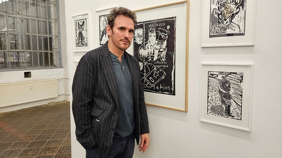 Matt Dillon, ein Mann steht in einer Ausstellung von gerahmten Grafiken.