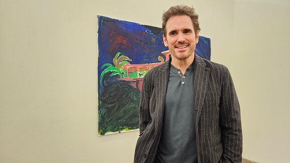 Matt Dillon, ein Mann steht vor einem Gemälde, das an einer Ausstellungswand hängt