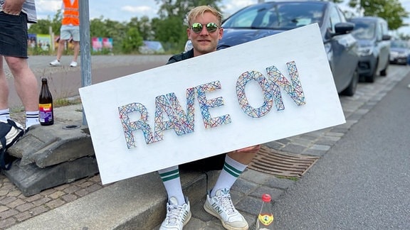 Ein Mann mit einem Plakat mit der Aufschrift "Rave on"