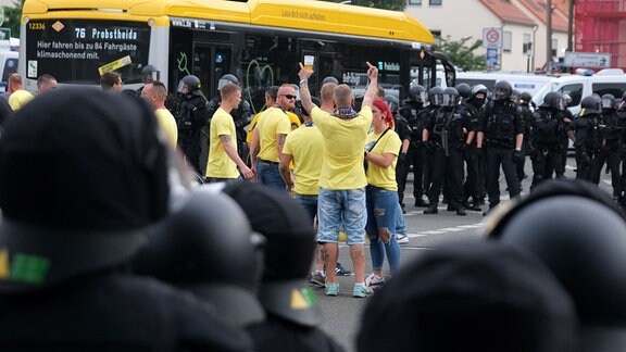 Fußballfans des 1. FC Lokomotive Leipzig stehen auf einer Kreuzung der Polizei gegenüber. 