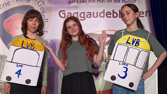 Drei Mädchen tragen selbst bebastelte Kostüme und schauen in die Kamera