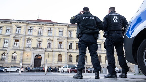 Zwei Polizisten, von hinten fotografiert, blicken auf ein Gerichtsgebäude.