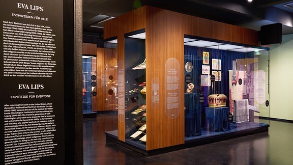 Ausstellungvitrinen mit vielen Objekten und Ausstellungstexte auf schwarzem Hintergrund sind zu sehen.