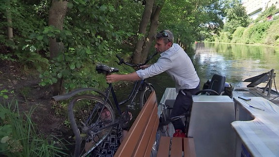 Der Leipziger Stadthafen-Geschäftsführer Jan Benzien hievt ein Schrott-Fahrrad von einem Kanalufer auf ein Boot.