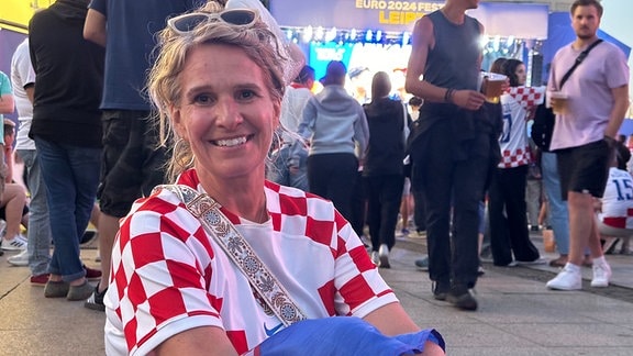 Eine Frau in einem Trikot der kroatischen Nationalmannschaft sitzt während des Fanfests in Leipzig auf dem Boden