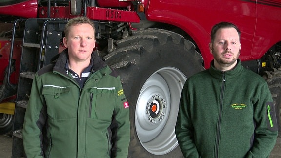 Zwei Männer mit grünlichen Jacken stehen vor einer Landmaschine