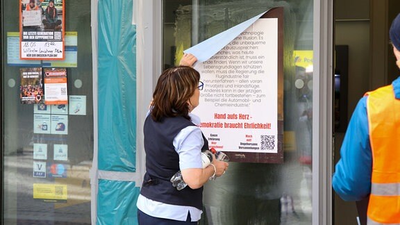 Eine Frau zieht ein Plakat von einer Glastür ab.