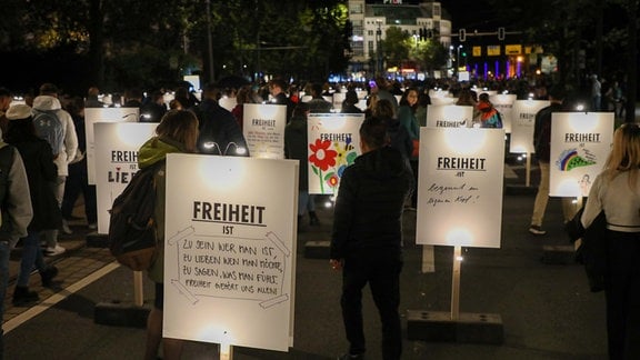 Auf dem Innenstadtring in Leipzig stehen beleuchtete Schilder, auf denen Menschhen ihre Meinung zu Demokratie und Freiheit geschrieben haben. Hunderte Menschen laufen daran vorbei und lesen die Aussagen.