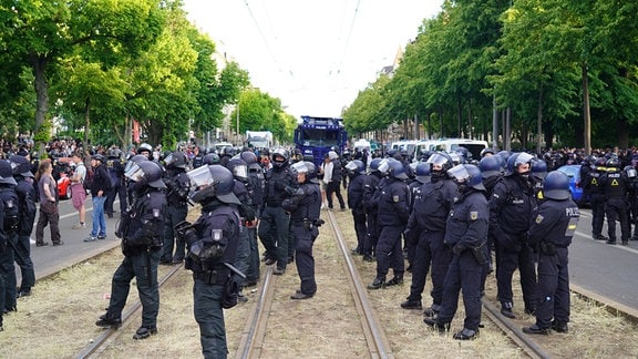 Polizisten stehen in der Mitte einer Straße, rechts und links sind Menschen.