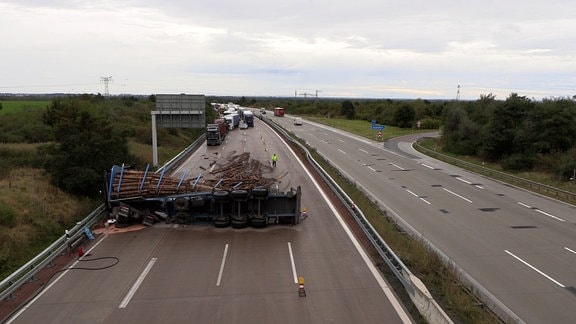 Ein Laster, gebladen mit Holzstämmen liegt quer auf einer Fahrbahn.