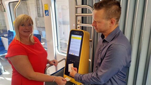 Eine Frau und ein Mann bedienen einen Ticketautomaten. 