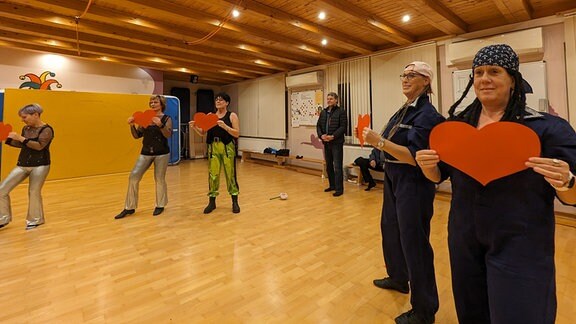 Frauen halten bei einer Tanzprobe Papierherzen hoch. 