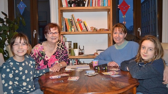 Mutter sitzt mit Oma und Enkelinnen gemeinsam an einem Tisch.