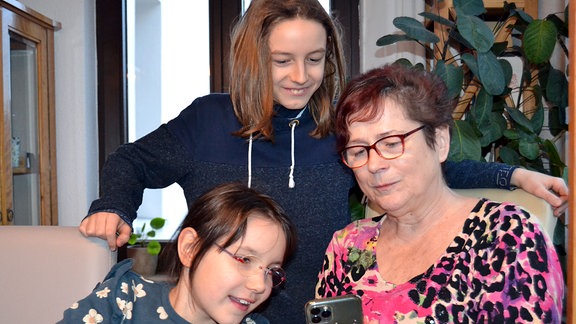 Oma und Enkelinnen schauen auf Smartphone.