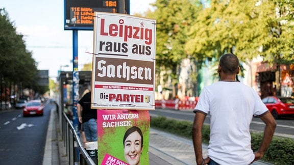 Ein Wahlplakat mit der Aufschrift "Leipzig raus aus Sachsen" von der Satirepartei "Die Partei" hängt über einem Plakat der Grünen an einer Straßenbahnhaltestelle in Leipzig