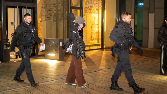 Eine junge Frau geht zwischen zwei Polizisten aus dem Uni-Gebbäude