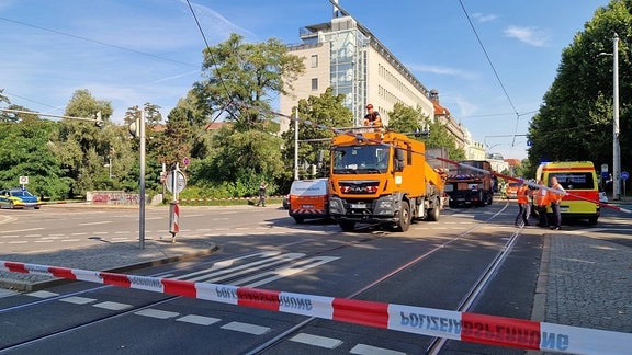 Ein rot-weißes Absperrband hängt vor einem orangenen LKW mit Hebebühne auf einer Straßenkreuzung.