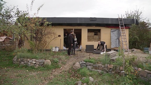 Mehrere Personen stehen vor einem Haus aus Strohballen und Holz. 